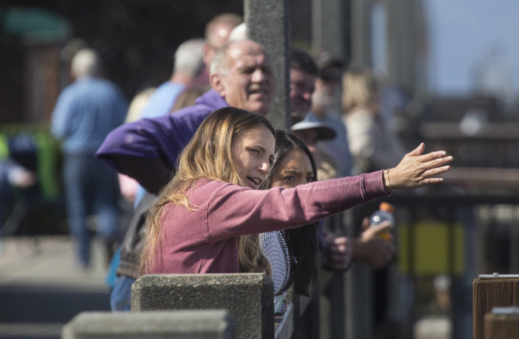 A woman explains to a friend how the bridge goes into place as they watch the installation from the marina pier while the Grand Avenue Park Bridge is slowly rotated into place along Marine View Drive on Wednesday in Everett. (Andy Bronson / The Herald)
