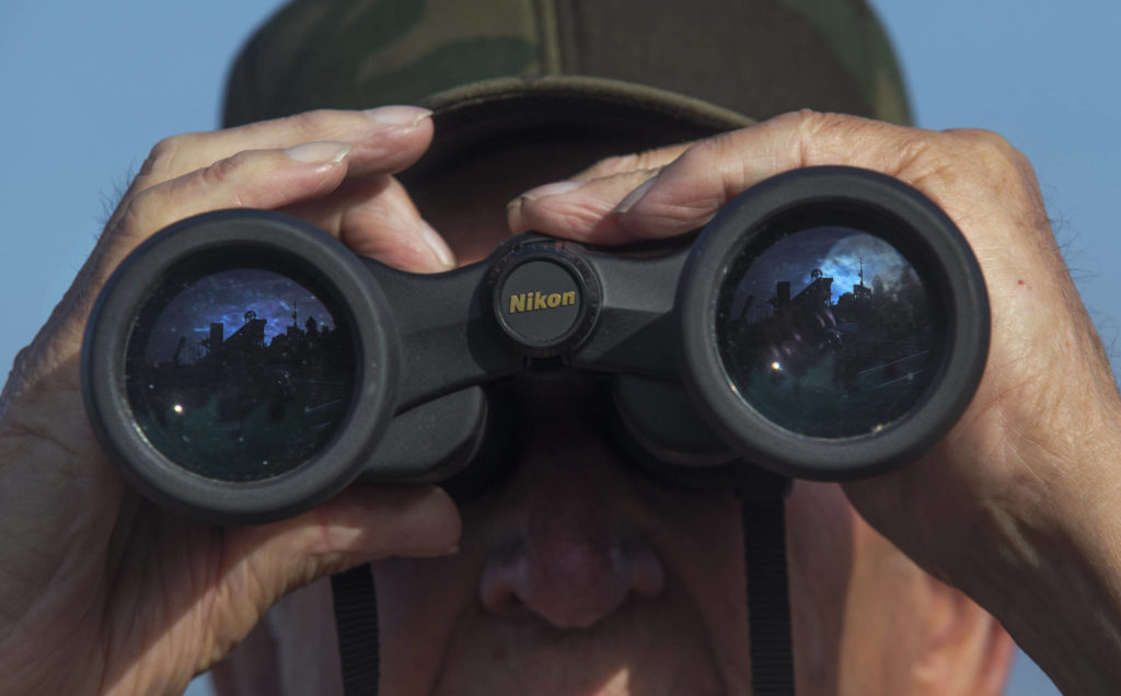 The Grand Avenue Park Bridge is reflected in Mack Hyatt’s binoculars as he waits for it to be rotated into place on Wednesday in Everett. (Andy Bronson / The Herald)
