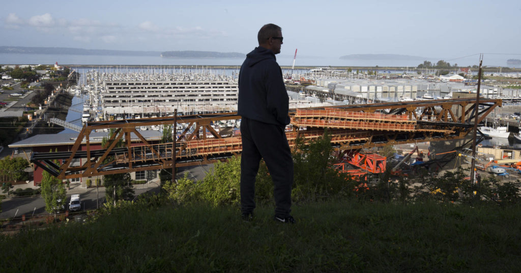 A man stands out on the bluff at Grand Avenue Park as the new pedestrian bridge is moved into place on Wednesday in Everett. (Andy Bronson / The Herald)
