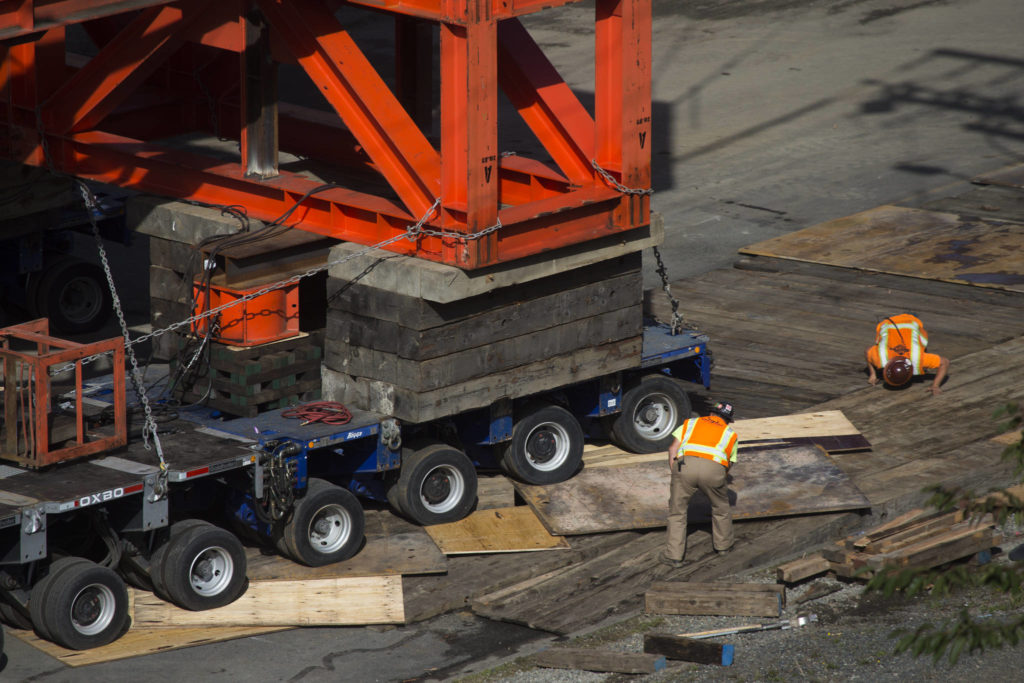 Workers peer under the wheels as the $20 million Grand Avenue Park Bridge rolls over dunnage to keep the wheels from sinking into the earth as it was slowly rotated into place along Marine View Drive on Wednesday in Everett. (Andy Bronson / The Herald)
