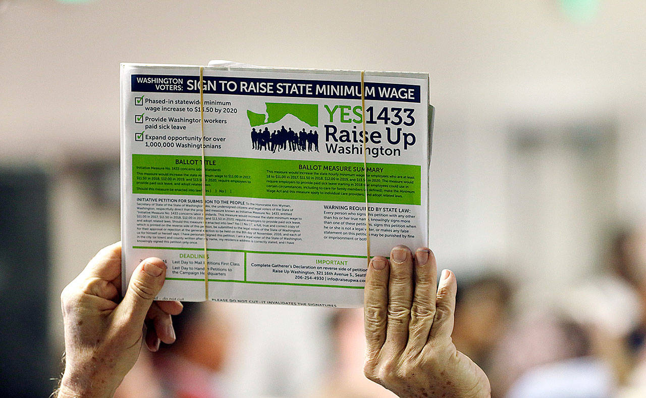 A supporter holds up a petition for Initiative 1433, a ballot measure to raise Washington state’s minimum wage and allow all workers in the state to earn paid sick leave, in Everett, in March 2016. The passage of the minimum wage increase was among the top news stories in Washington in 2016. (Elaine Thompson /Associated Press file photo)