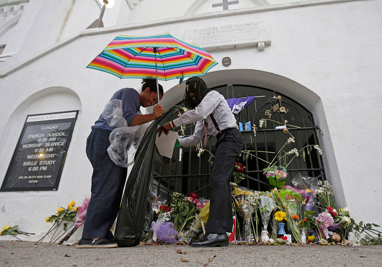 Barrye Browne (left) and Daron Calhoun collect memorials placed at Mother Emanuel AME Church in Charleston, S.C., on July 17, 2016, the first anniversary of the killing of nine black parishioners during bible study. The gunman who killed the worshippers had been arrested on drug charges just weeks prior to the shooting. Although that arrest should have prevented him from purchasing the pistol he used in the attack, the examiner reviewing the sale never saw the arrest report because the wrong agency was listed in state criminal history records. (Chuck Burton / Associated Press file photo)