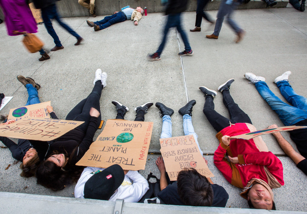 Students from ACES Alternative High School in Mukilteo participate in the “die-in” during the Global Climate Strike as people walk by at the Snohomish County Campus Plaza on Friday in Everett. (Olivia Vanni / The Herald)
