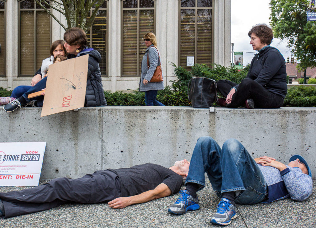 A passerby looks out at protestors participating in the “die-in” for climate action at the Snohomish County Campus Plaza on Friday in Everett. (Olivia Vanni / The Herald)
