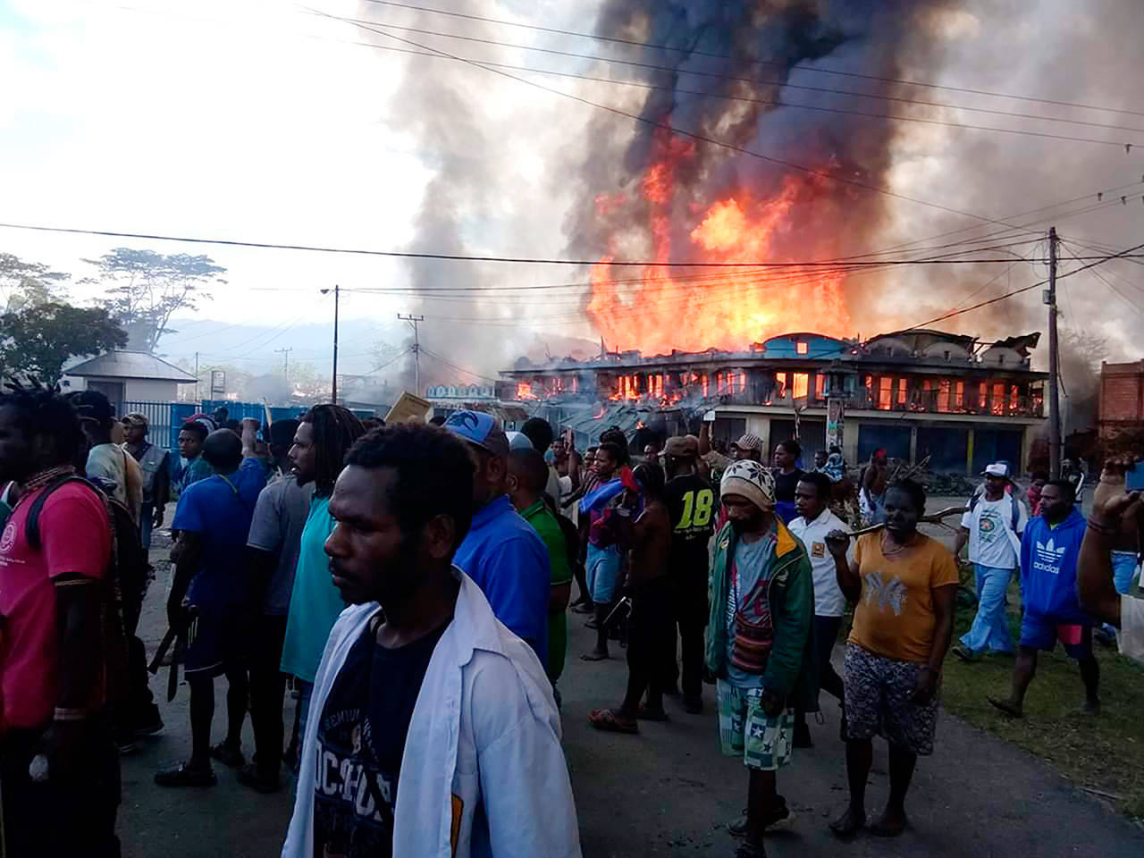 People gather as shops burn Monday in the background during a protest in Wamena in Papua province, Indonesia. Hundreds of protesters in Indonesias restive Papua province set fire to homes and other buildings Monday in a protest sparked by rumors that a teacher had insulted students, and a soldier was killed in another protest in the region, police said. (AP Photo)
