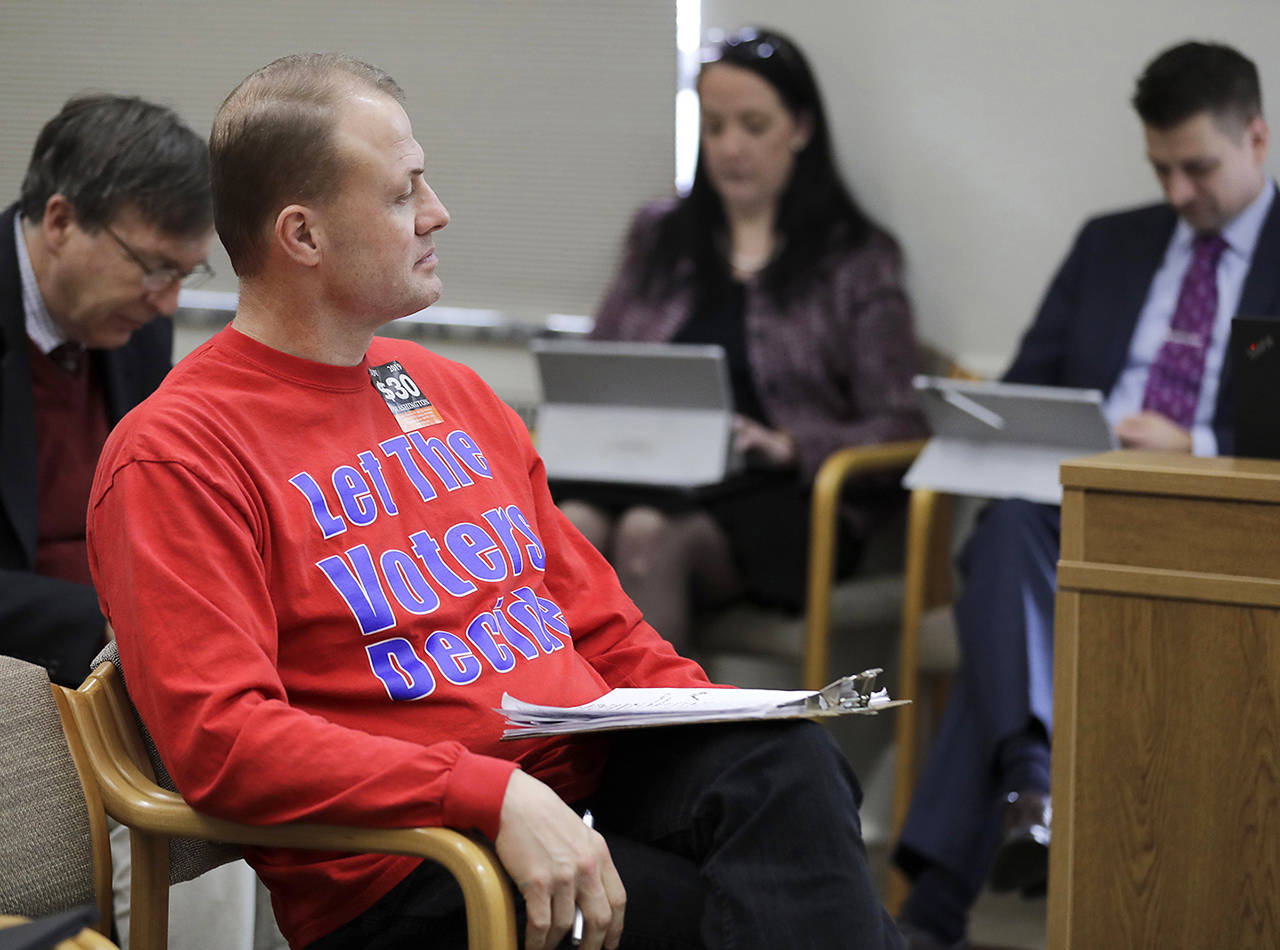 In this Feb. 13 photo, anti-tax initiative promoter Tim Eyman (center) waits before speaking during a public hearing at the Capitol in Olympia. (AP Photo/Ted S. Warren, file)