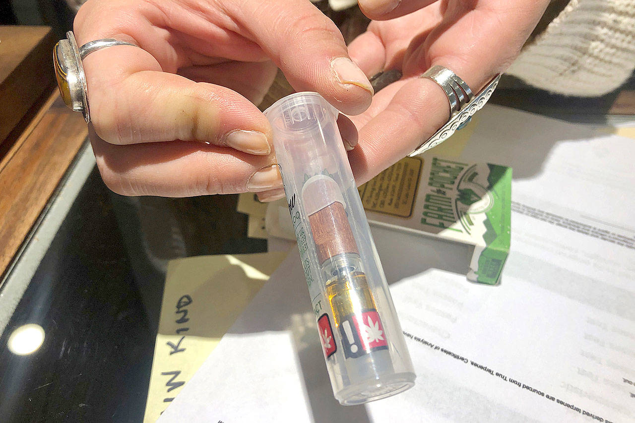 Cameron Moore, general manager of Bridge City Collective in Portland, Oregon, holds a vape cartridge that’s on sale at the dispensary Sept. 20. The company had a 31% drop in sales of vape cartridges that hold the oil that vaporizes when heated. Vaping products are taking a hit as health experts scramble to determine what’s causing a mysterious lung disease. (AP Photo/Gillian Flaccus)