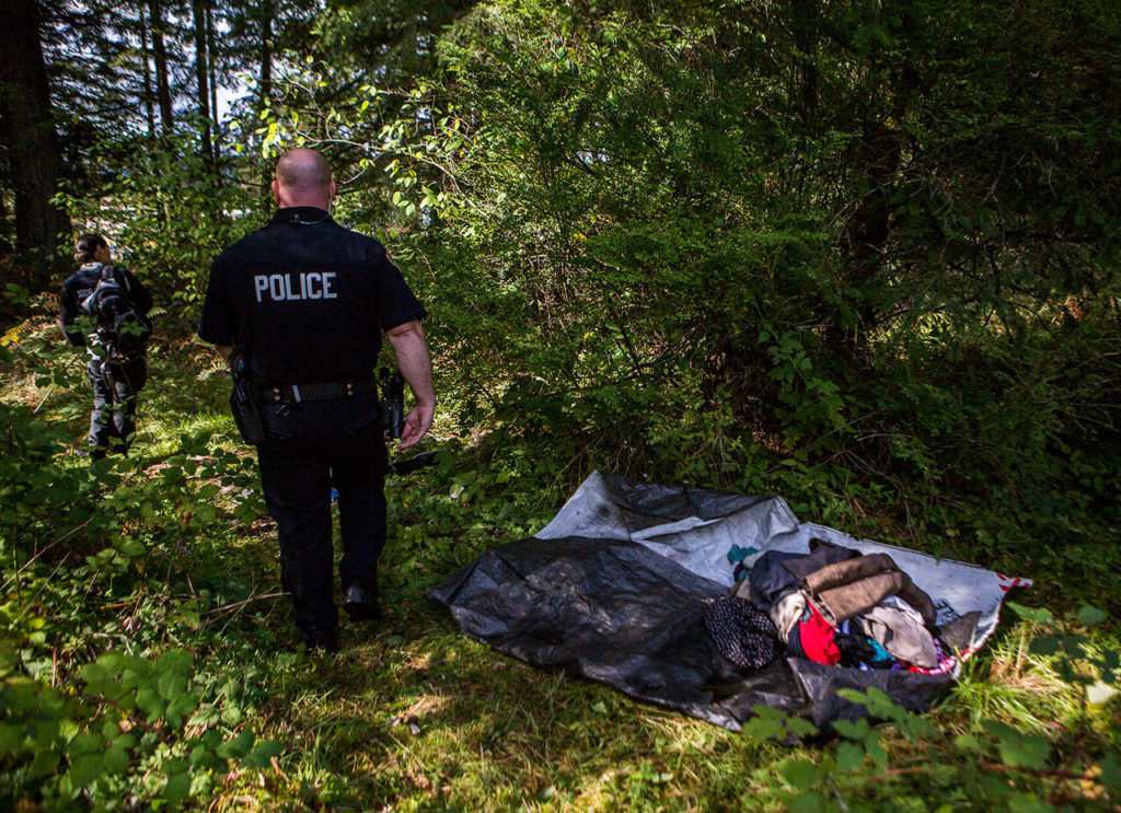 Social worker Elisa Delgado (left) and Officer Justin Springer (right) walk through a recently cleared out homeless encampment on Thursday in Monroe. (Olivia Vanni / The Herald)
