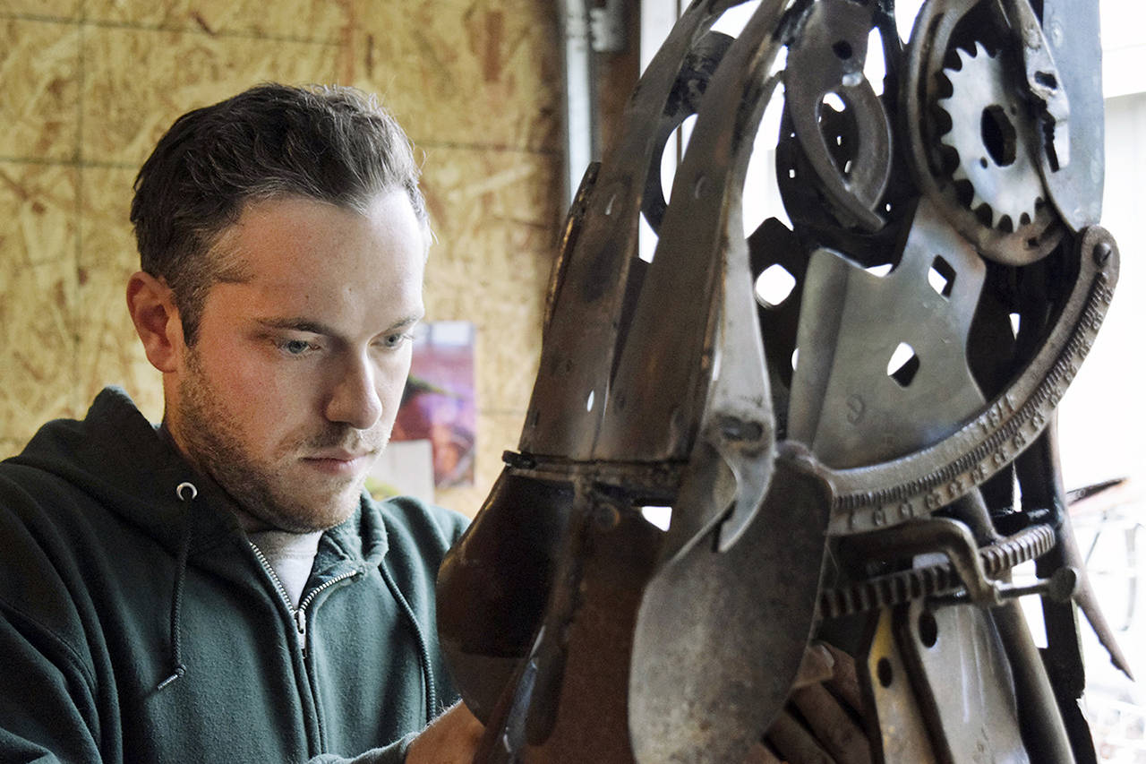 In his Clinton garage studio, Aidan Rayner works on his howling wolf sculpture comprising discarded machine parts, tools and other metal found at Island Recycling. The artwork is slated to be a memorial for his twin brother, Dylan Rayner, who died in 2016. (Patricia Guthrie / South Whidbey Record)