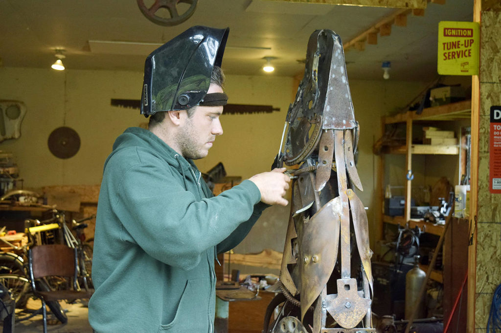 In his Clinton garage studio, Aidan Rayner works on his howling wolf sculpture comprising discarded machine parts, tools and other metal found at Island Recycling. The artwork is slated to be a memorial for his twin brother, Dylan Rayner, who died in 2016. (Patricia Guthrie / South Whidbey Record)
