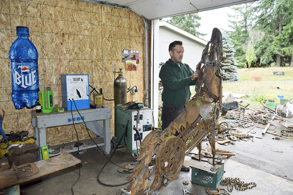 In his Clinton garage studio, Aidan Rayner works on his howling wolf sculpture comprising discarded machine parts, tools and other metal found at Island Recycling. The artwork is slated to be a memorial for his twin brother, Dylan Rayner, who died in 2016. (Patricia Guthrie / South Whidbey Record)
