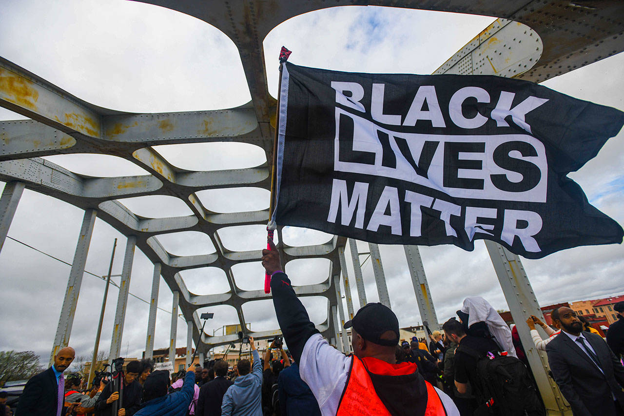 A Black Lives Matter demonstrator waves a flag on the Edmund Pettus Bridge during the Bloody Sunday commemoration in Selma, Alabama, on March 3. Majorities of Americans across racial lines say white people are treated more fairly than black people by the police, according to a new poll from The Associated Press-NORC Center for Public Affairs Research. The dynamic has played out in the wake of the Black Lives Matter movement, which began in 2014 with the fatal shooting of unarmed 18-year-old Michael Brown by white, former Ferguson, Missouri, police officer Darren Wilson. (AP Photo/Julie Bennett, File)