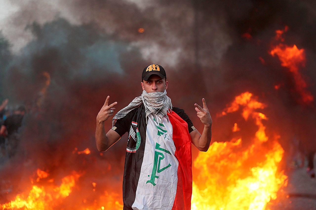 An anti-government protester flashes the victory sign during a demonstration, in Baghdad, Iraq, Thursday. Iraqi security forces fired live bullets into the air and used tear gas against a few hundred protesters in central Baghdad on Thursday, hours after a curfew was announced in the Iraqi capital on the heels of two days of deadly violence that gripped the country amid anti-government protests that killed over 19 people in two days. (AP Photo/Hadi Mizban)