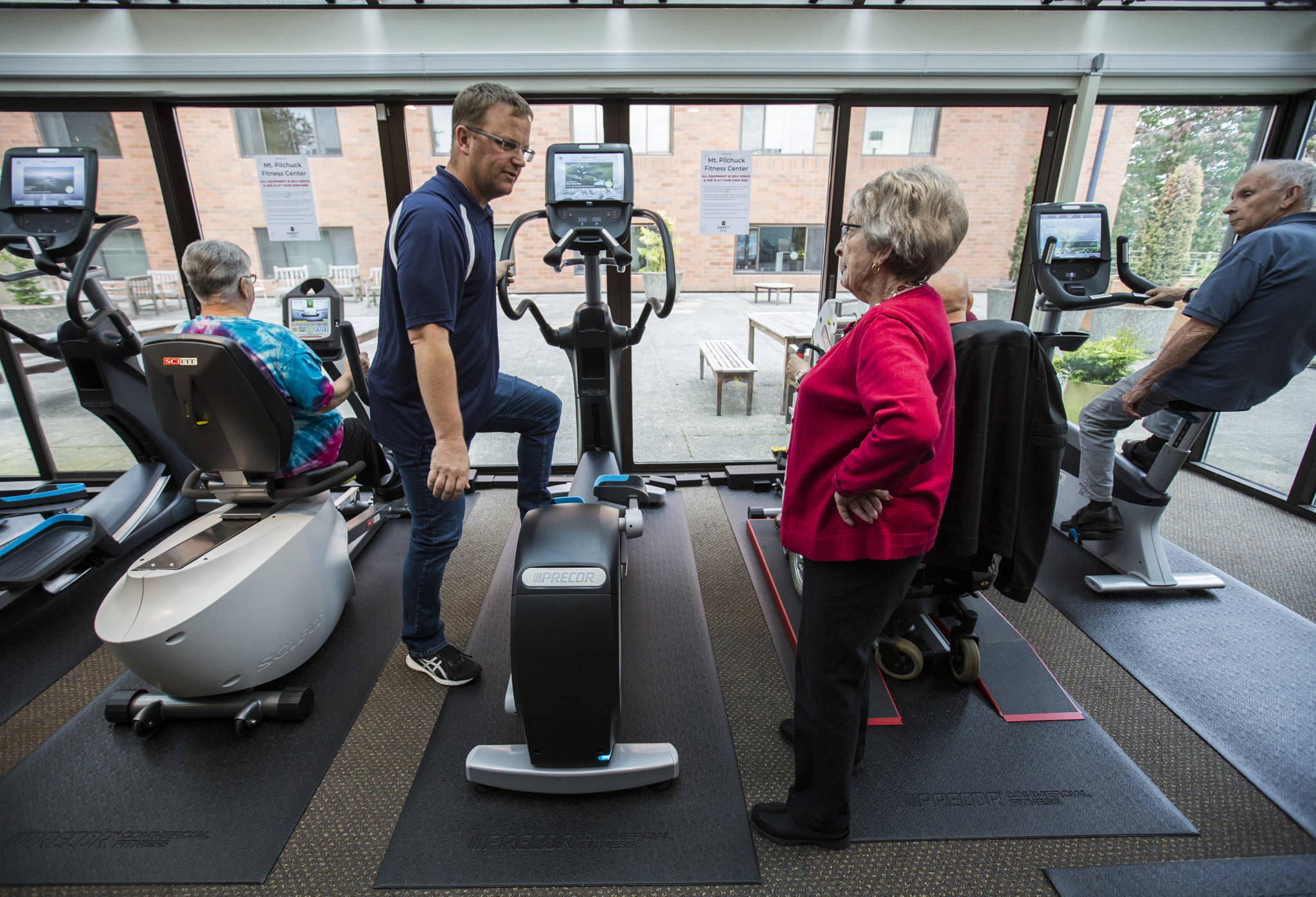 Program coordinator Eric Wollan (left) explains to Doris Moran how to use the elliptical machine at the Carl Gipson Senior Center’s new fitness room in Everett. (Olivia Vanni / The Herald)