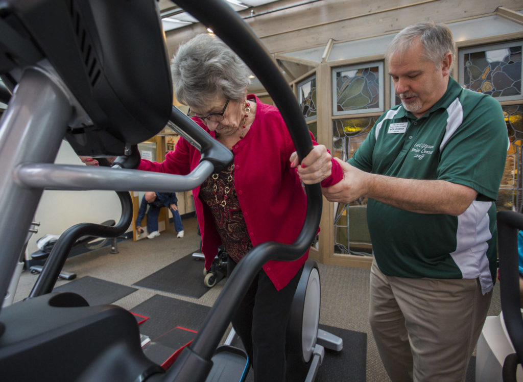 Bob Dvorak helps Doris Moran onto the elliptical at the Carl Gipson Senior Center’s new fitness room. (Olivia Vanni / The Herald)
