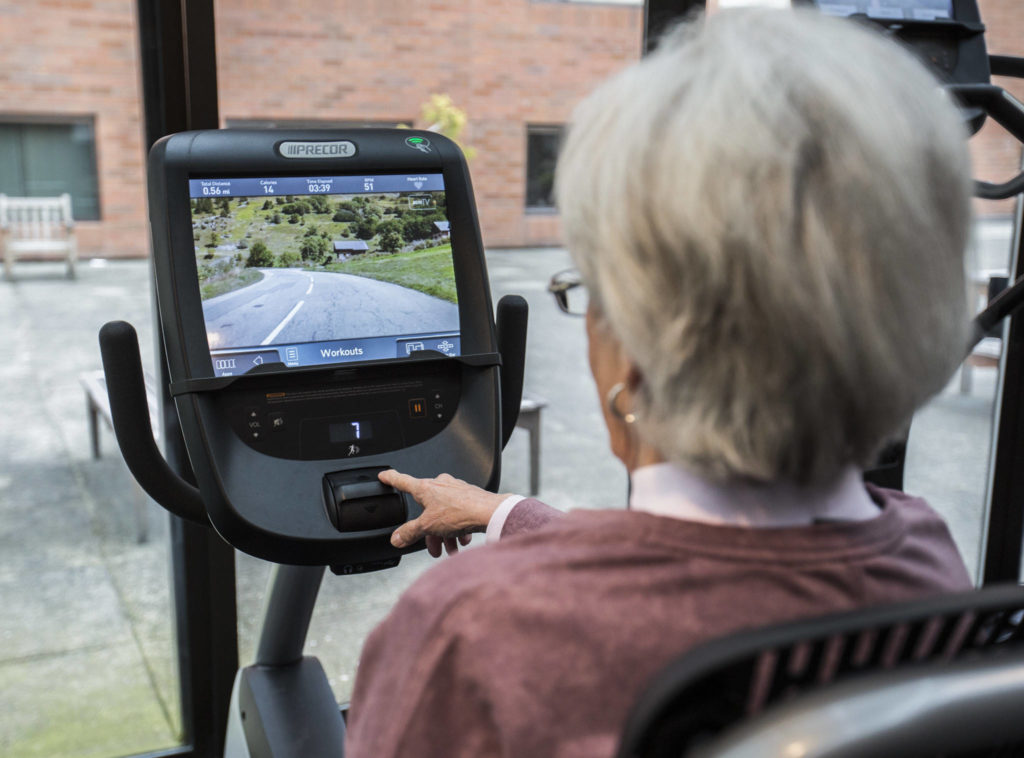A screen screen shows a video of mountain road that moves at the same pace as your pedaling at the Carl Gipson Senior Center’s new fitness room. (Olivia Vanni / The Herald)
