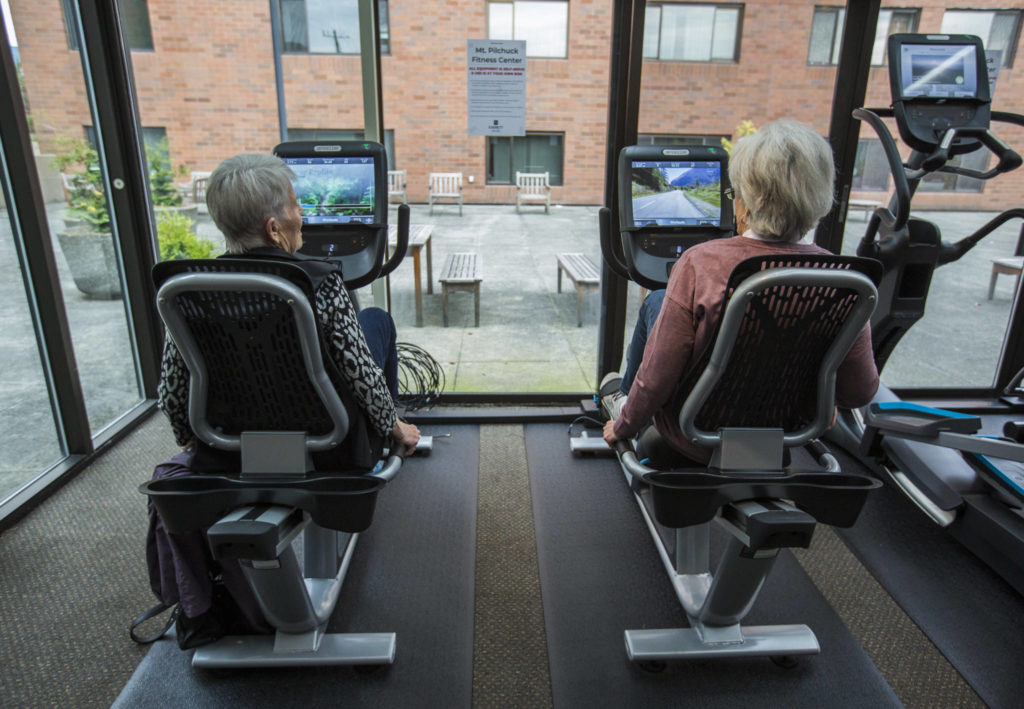 Jean Kinity (left) and Sandra Barton chat as they try out the new recumbent bikes at the Carl Gipson Senior Center’s new fitness room. (Olivia Vanni / The Herald)
