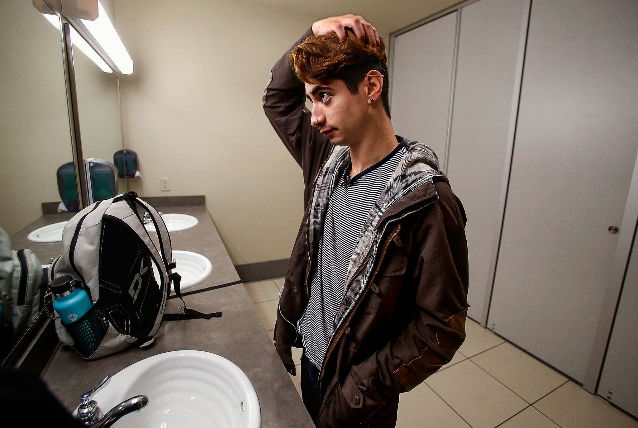 Humberto Villarruel, a 21-year-old Everett Community College student, uses the mirror in an all-gender restroom in the Parks Student Union on campus Tuesday. (Dan Bates / The Herald)