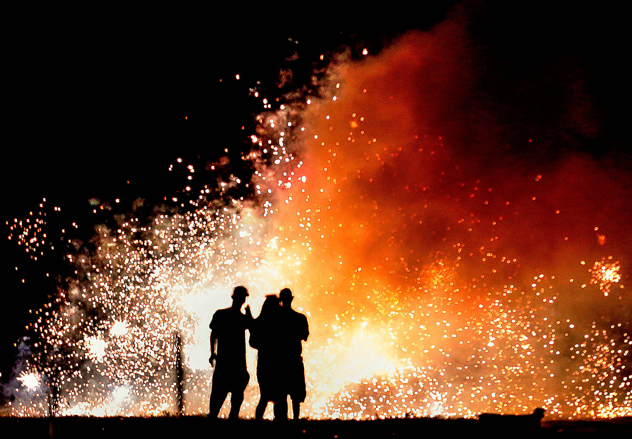 In a large area reserved for setting off fireworks in Tulalip, a trio of enthusiasts watch a shower of sparks June 26, 2018, as darkness falls at Boom City, the seasonal retail area on the Tulalip Indian Reservation. The Snohomish County Council wants to know how voters feel about a proposed fireworks use ban in unincorporated areas of Snohomish County, which would exclude Tulalip. (Dan Bates / The Herald)