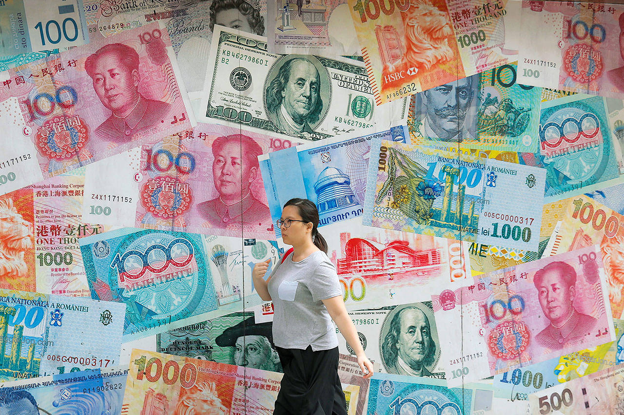 A woman walks by a money exchange shop Aug. 6 that is decorated with different countries currency banknotes at Central, a business district in Hong Kong. The IMF’s latest World Economic Outlook comes on the eve of meetings in Washington this week of the IMF and its sister lending organization, the World Bank. (AP Photo/Kin Cheung, File)