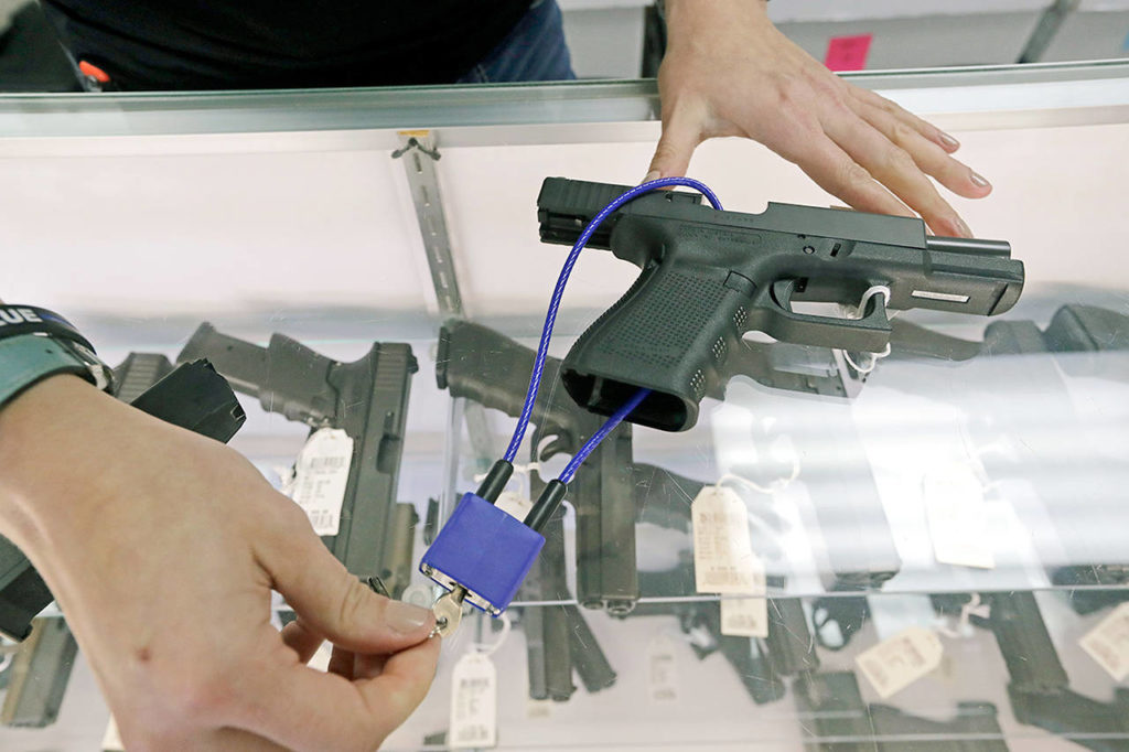 In this photo taken in October 2018, gun shop owner Tiffany Teasdale demonstrates how a gun lock works on a handgun in Lynnwood. Voters in Washington state approved an initiative last year that toughened background checks for people buying semi-automatic rifles, increased the age limit to 21 for buyers of those guns and required safe storage of all firearms. A firearms storage law in Edmonds was ruled against Friday in Snohomish County Superior Court. (AP Photo/Elaine Thompson)
