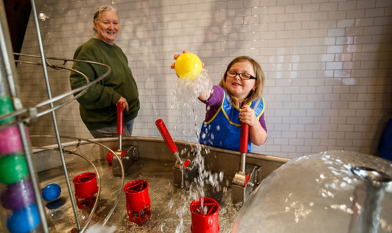 In this March 2018 photo, Madison Davis of Snohomish reaches into the air pocket of a water feature at the Imagine Children’s Museum in Everett, while her “adopted grandmother” Michele Tanis watches. (Dan Bates / Herald file)