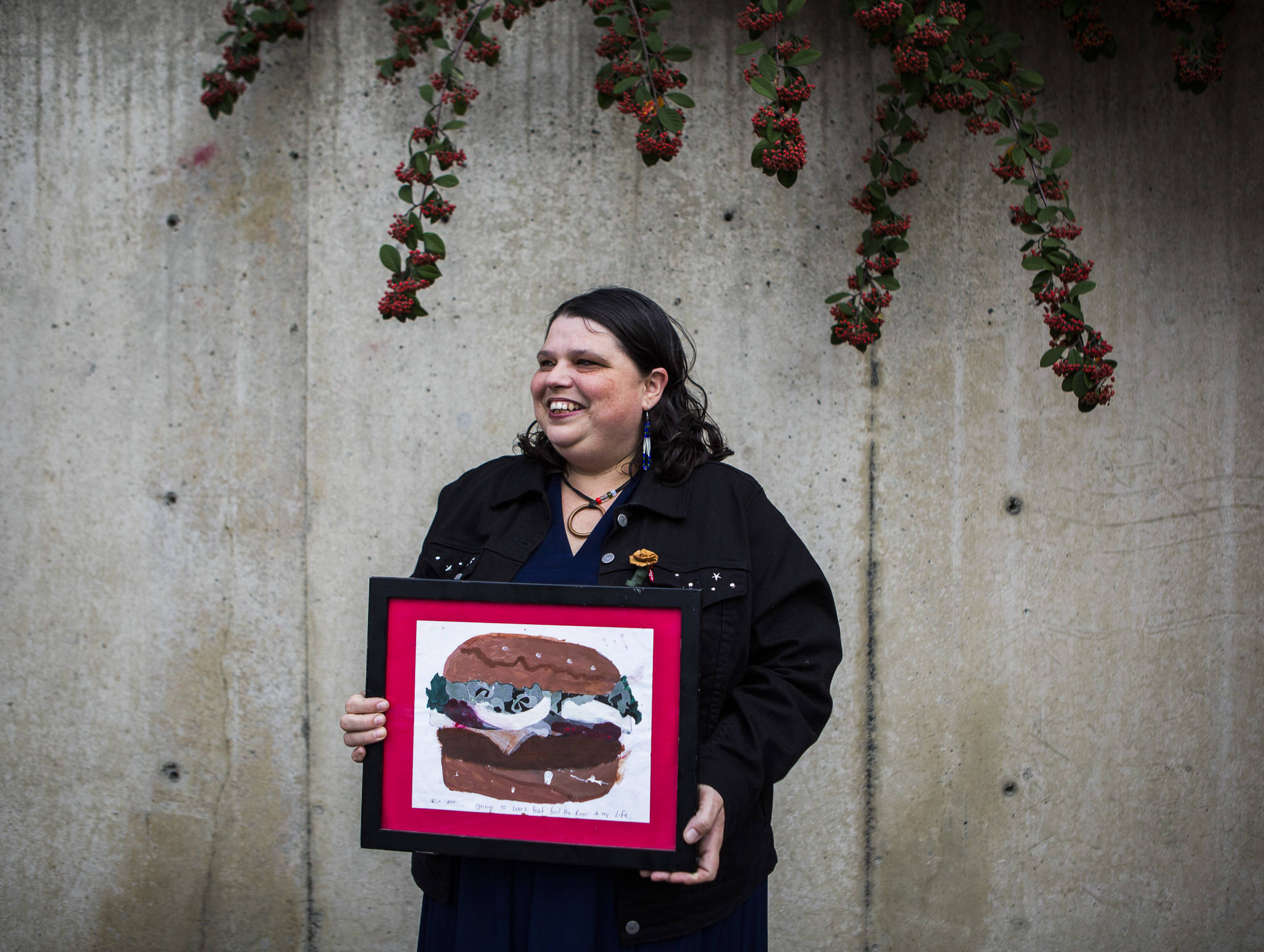 Maizy Brown holds a painting she made of a burger with the phrase “I’m not going to work fast food for the rest of my life” underneath it as motivation while she attended school. Brown now counsels students at Edmonds Community College. (Olivia Vanni / The Herald)