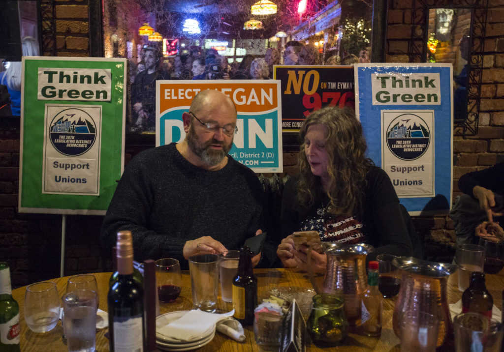 Bill Sheets and Ardis Hallanger are surrounded by signs as they check their phones as the first numbers come in on election night at the Vintage Cafe in Everett. (Olivia Vanni / The Herald)
