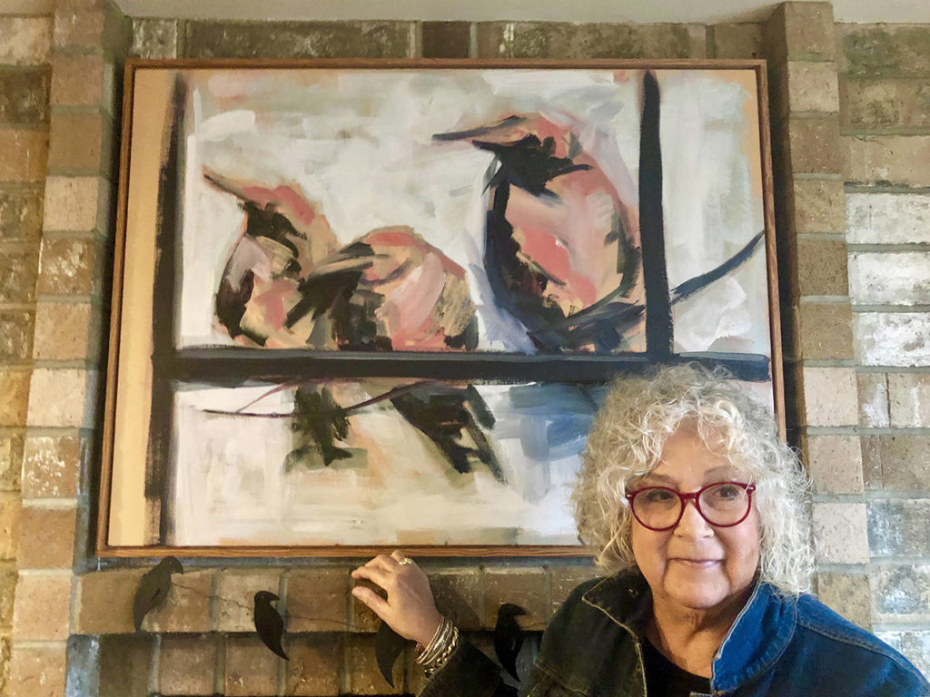 Sharen Heath stands in front of the crow painting that sparked her obsession to collect birds in various forms and put some giant ones in the front yard of her Langley home. (Andrea Brown / The Herald)
