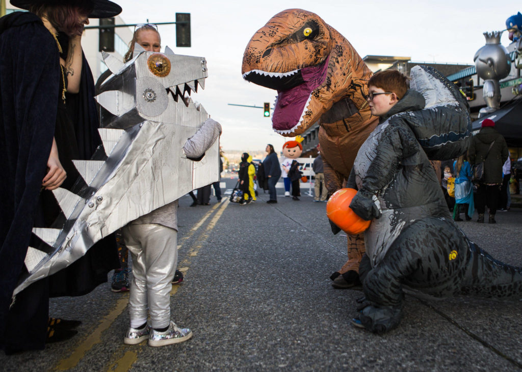 A group of people in dinosaur costumes greet each other during Downtown Trick-or-Treating on Oct. 31, 2019 in Everett, Wash. (Olivia Vanni / The Herald)
