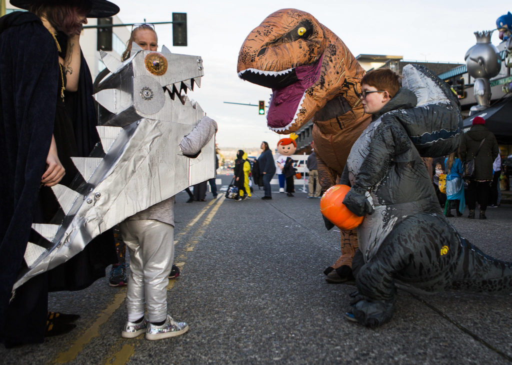 A group of people in dinosaur costumes greet each other during Downtown Trick-or-Treating on Oct. 31, 2019 in Everett, Wash. (Olivia Vanni / The Herald)