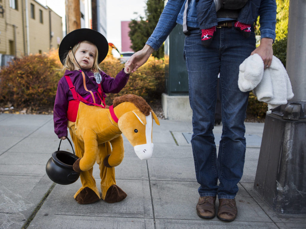 Tessa Deurbrouck, 2, holds her mothers hands while they walk along California Street during Downtown Trick-or-Treating on Oct. 31, 2019 in Everett, Wash. (Olivia Vanni / The Herald)
