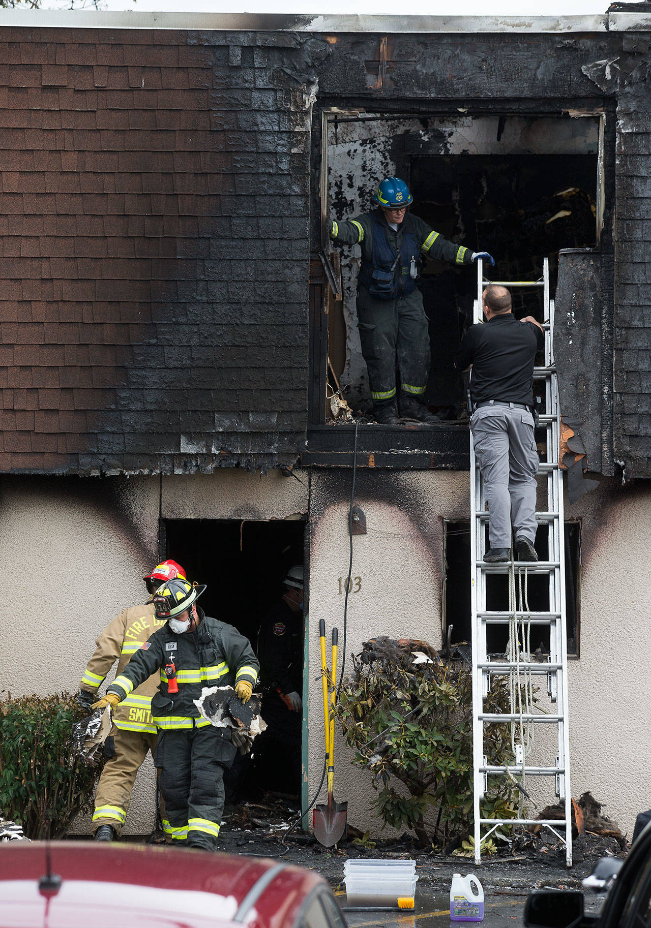 Fire investigators, right, talk as firefighters remove debris after a fatal fire at 6707 196th St. SW on Monday in Lynnwood. (Andy Bronson / The Herald)