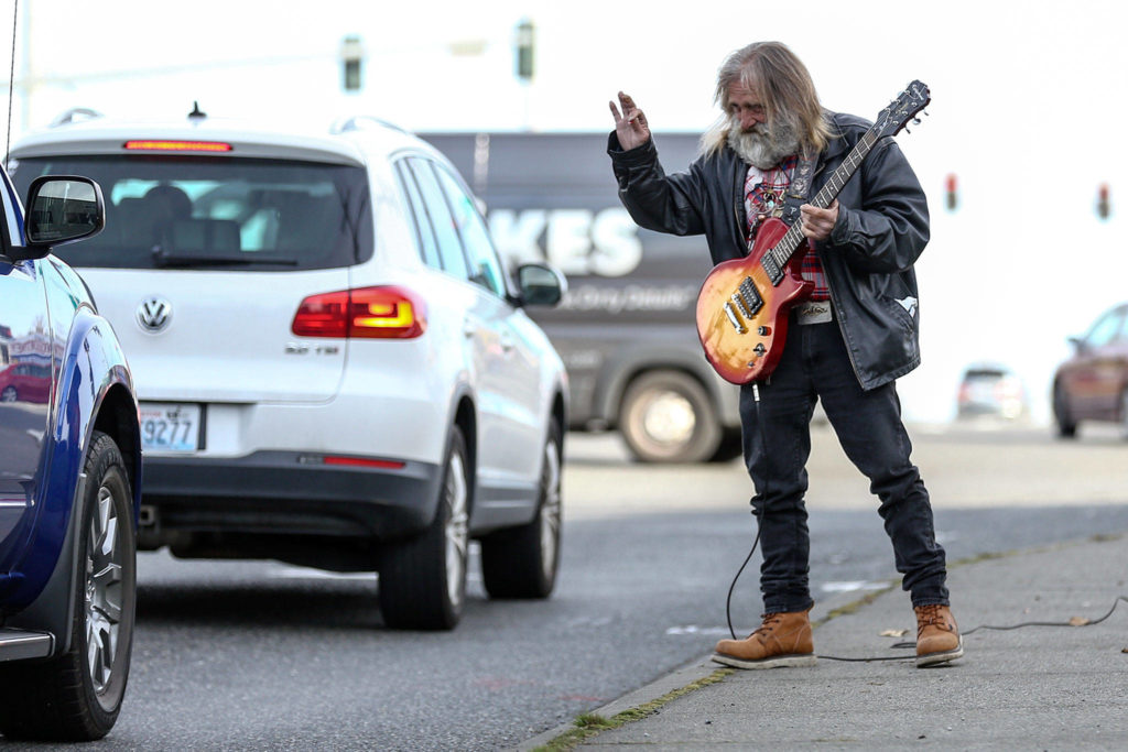 Jim Morris, also known as Wolfman Jim, a longtime panhandler, waves to drivers in Lynnwood. Drunk and homeless for decades, he now performs his act clean and sober. (Kevin Clark / The Herald)
