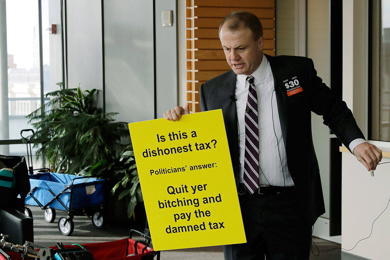 Anti-tax activist Tim Eyman holds a sign as he prepares to talk to reporters Thursday outside the office of Seattle Mayor Jenny Durkan in Seattle. (AP Photo/Ted S. Warren)