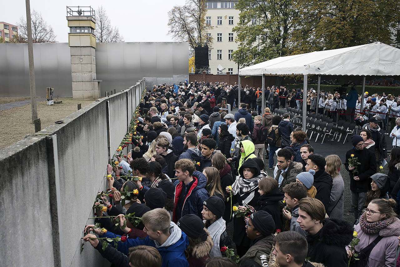 Young people stuck flowers in remains of the Berlin Wall during a commemoration ceremony to celebrate the 30th anniversary of the fall of the Berlin Wall at the Wall memorial site at Bernauer Strasse in Berlin on Saturday. (AP Photo/Markus Schreiber)