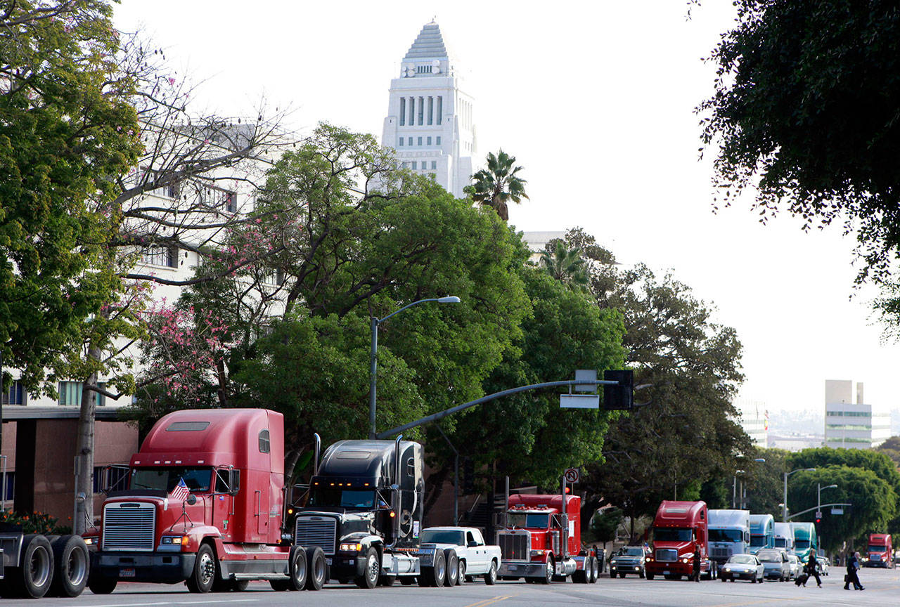 In this Friday, Nov. 13, 2009 file photo a caravan of trucks from the ports of Los Angeles and Long Beach, Calif., drive around Los Angeles City Hall during a protest against container fees being assessed against independent truckers. The California Trucking Association has filed what appears to be the first lawsuit challenging a sweeping new labor law that seeks to give wage and benefit protections to workers in the so-called gig economy, including rideshare drivers at companies such as Uber and Lyft. The federal lawsuit filed Tuesday contends that the legislation violates federal law and would deprive more than 70,000 independent truckers’ of their ability to work. (AP Photo/Damian Dovarganes, File)
