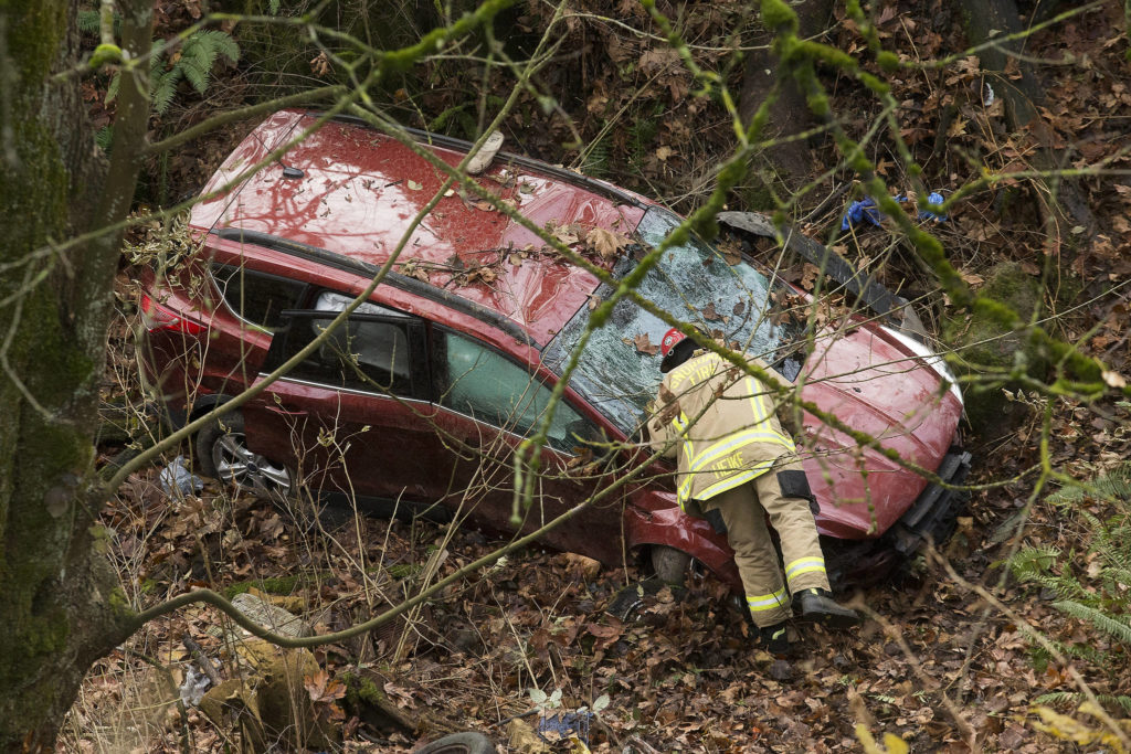 A Snohomish County firefighter peers into a vehicle after the driver crashed the car into a ravine. (Andy Bronson / The Herald)
