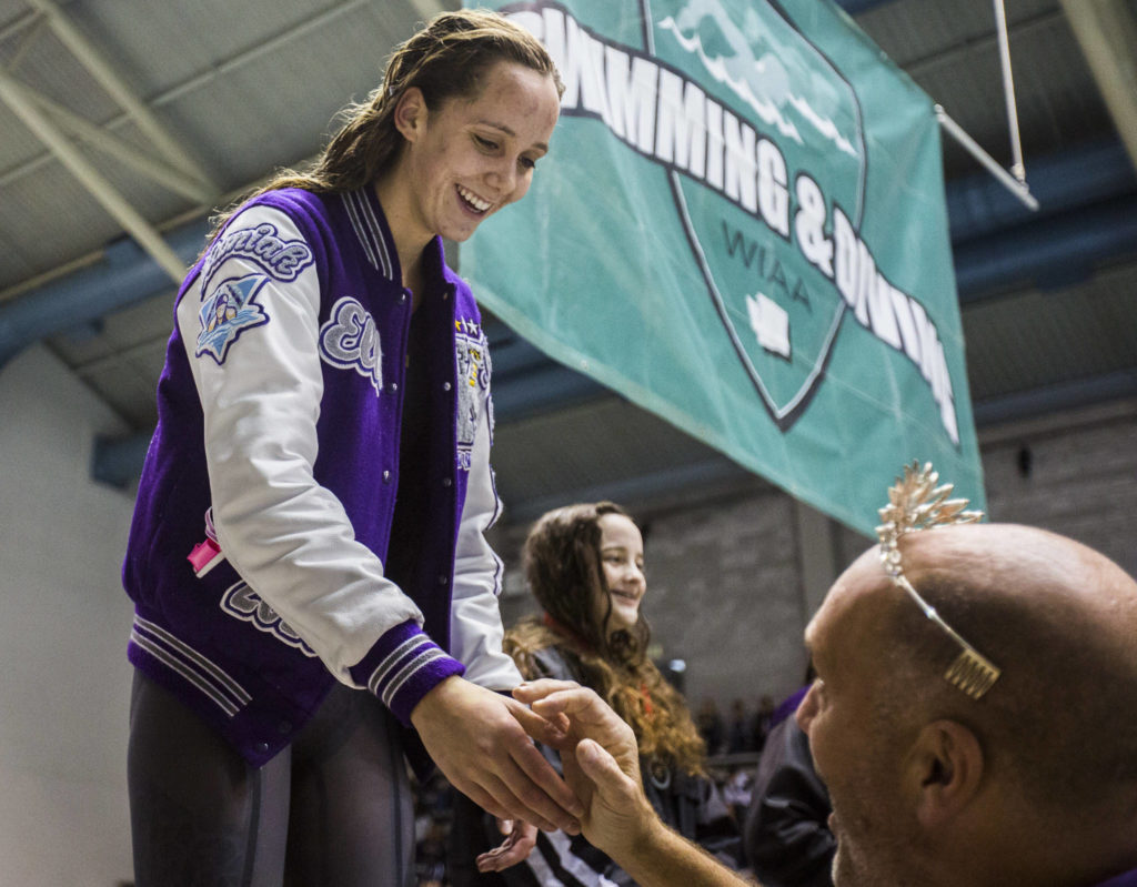 Kamiak senior Elli Straume smiles and shakes hands with coach Chris Erickson as she stands on the podium following her 200 freestyle triumph. (Olivia Vanni / The Herald)
