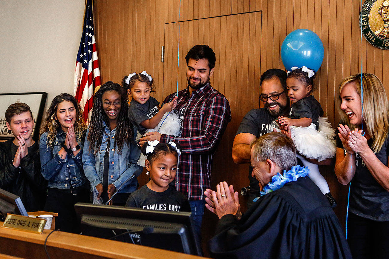 Arlington’s Avellaneda family join Judge David Kurtz at his bench as Mayah, 6, strikes his gavel Friday, National Adoption Day. Mayah and her two younger sisters, Alayna, 2, and Malaya, 1, were adopted by Jen (right) and Cid Avellaneda (next to Jen). Other family members are (from left) the Avellanedas’ son-in-law, Blake King, their daughter, Mariah King, their other adopted daughter, Nicole, 13, and their son, Jeriah Avellaneda, 26, holding Alayna. (Dan Bates / The Herald)