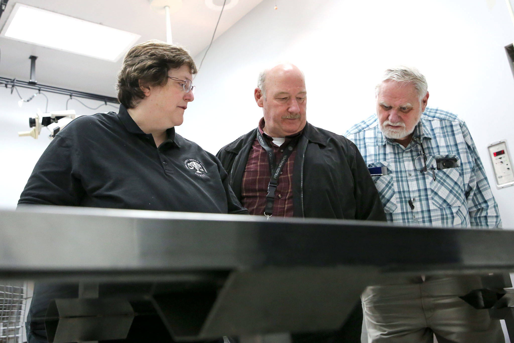 Kathy Taylor, a forensic anthropologist with the King County Medical Examiner’s Office (left), detective Jim Scharf of the Snohomish County Sheriff’s Office (center) and mental health professional Chuck Wright look over bones on a table Nov. 13, 2018, at the Snohomish County Medical Examiner’s Office. (Kevin Clark / Herald file)