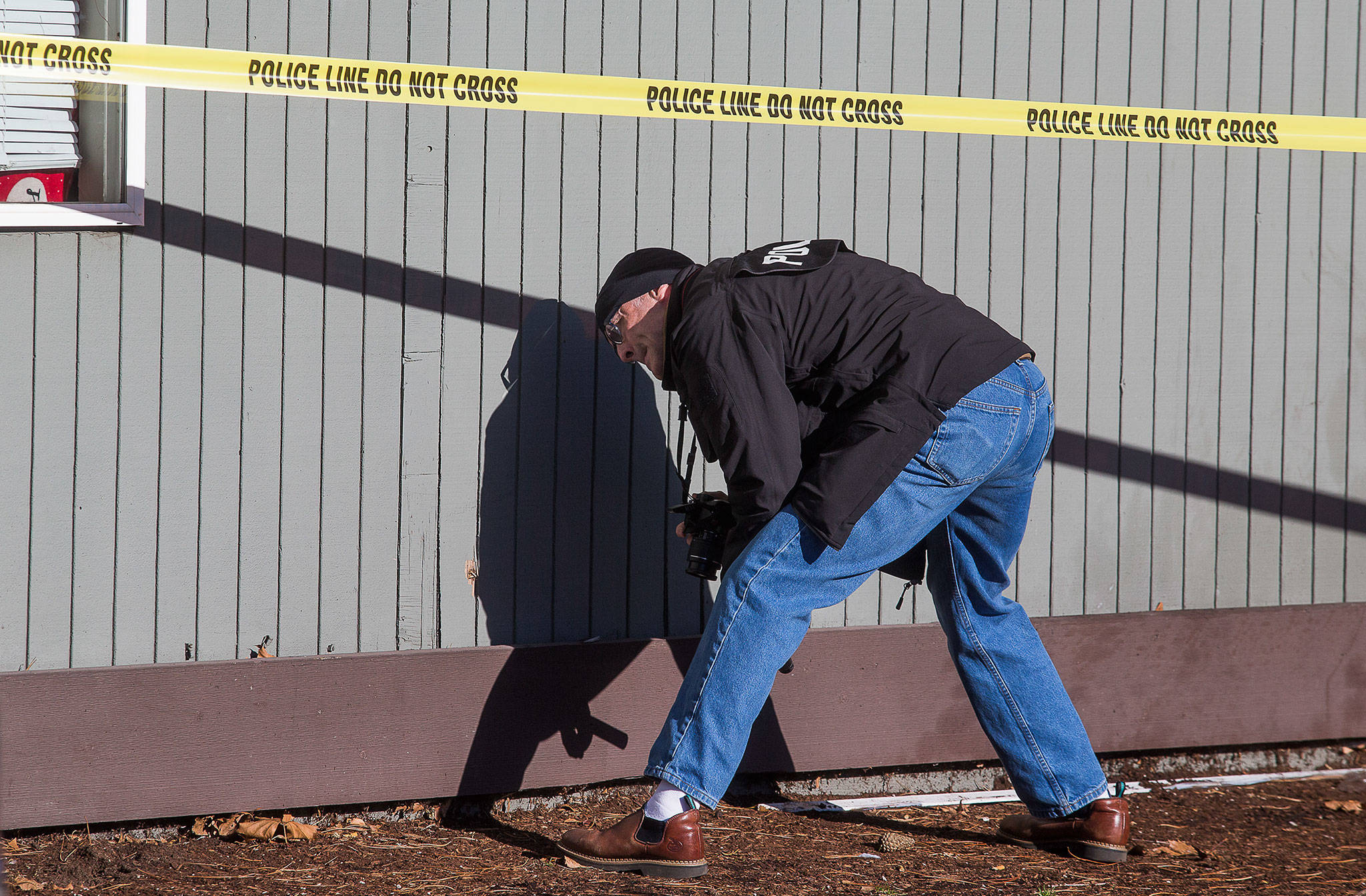 Everett Detective Randy Marrs looks at and takes photos of damage to a building, where gunfire wounded four people, one critically, on W. Casino Road on Thursday in Everett. (Andy Bronson / The Herald)