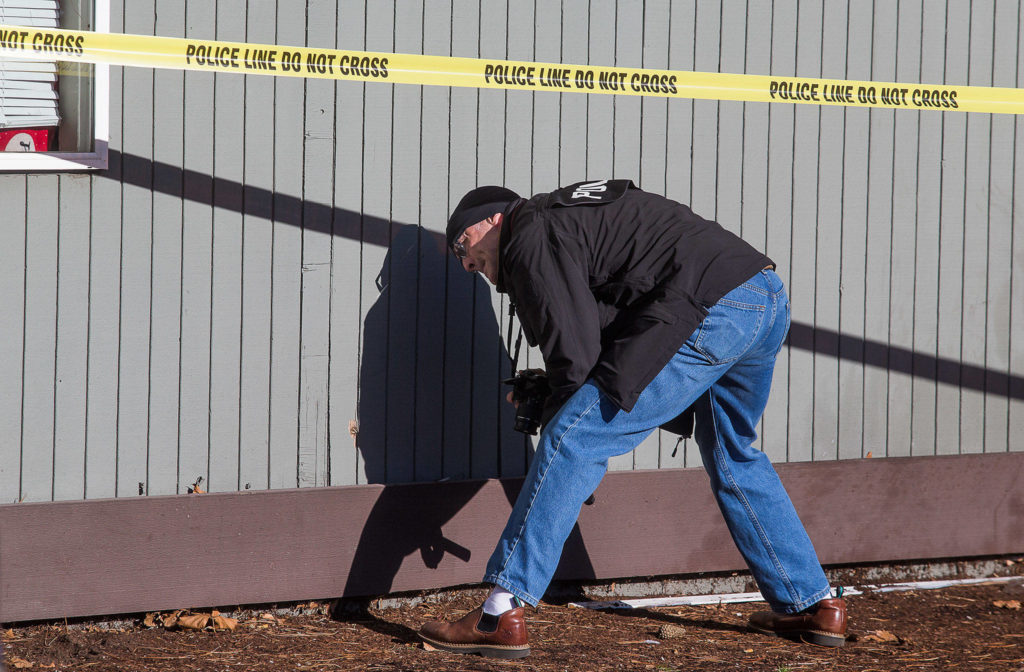 Everett Detective Randy Marrs looks at and takes photos of damage to a building, where gunfire wounded four people, one critically, on W. Casino Road on Thursday in Everett. (Andy Bronson / The Herald)
