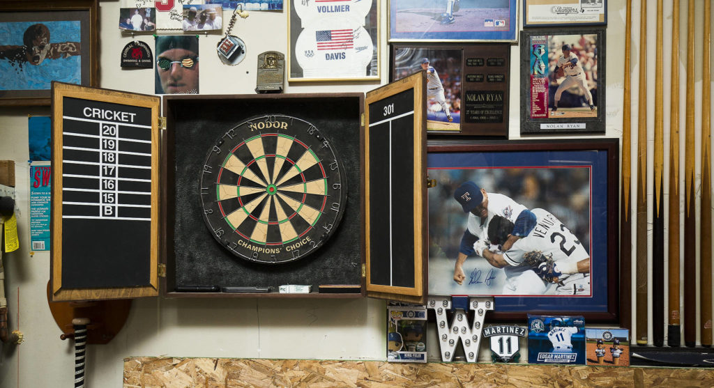 Pictures of Baseball Hall of Fame pitcher Nolan Ryan and swimming memorabilia surround a dartboard made by Josh Whall’s father. (Andy Bronson / The Herald)
