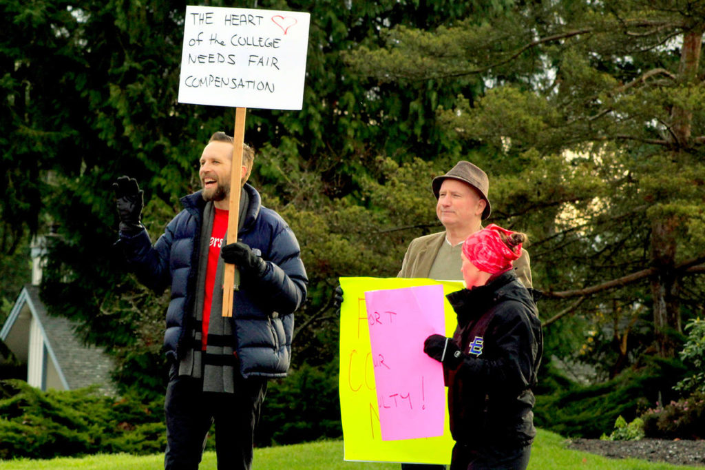 Pre-college English teacher Daniel Griesbach (left) waves to passing drivers during a demonstration outside the Edmonds Community College campus in Lynnwood on Tuesday. (Joey Thompson / The Herald)
