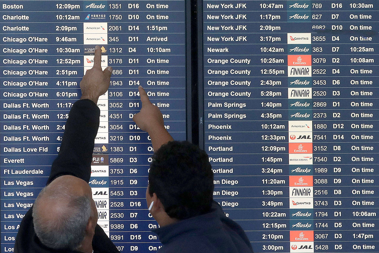 Two men point toward plane arrivals on a flight information board at San Francisco International Airport in San Francisco on. Northern California and southern Oregon residents are bracing for a “bomb cyclone” that’s expected at one of the busiest travel times of the year. (AP Photo/Jeff Chiu)