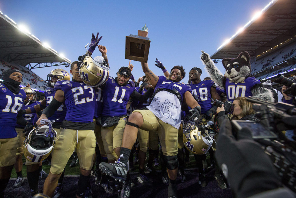 Washington players celebrate with the Apple Cup trophy after beating Washington State 31-13 in the 112th edition of the rivalry game Friday at Husky Stadium in Seattle. (Andy Bronson / The Herald)
