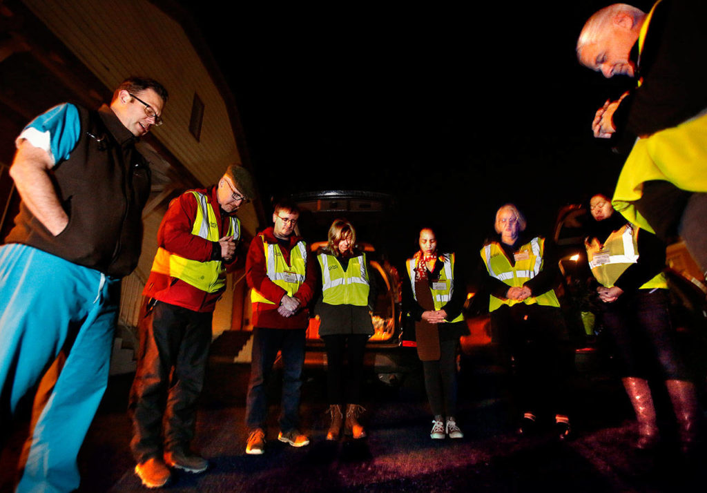 MercyWatch volunteers pray together in an Everett church parking lot before heading out to offer food, supplies and medical care to people living on the streets. From left are Dr. Jimmy Grierson, Deacon Dennis Kelly, Rodney Wagar, Sheri Dehaan, Ann Salonen, Gail Pyper, Amanda Dahl and Duane Schireman. (Dan Bates / The Herald)
