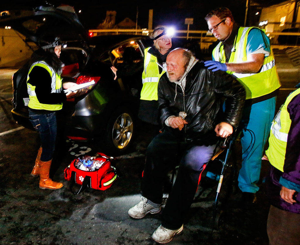 A man in a walker gets medical attention from MercyWatch volunteers Dr. Jimmy Grierson (right) and nurse Gail Pyper while medical scribe Amanda Dahl takes down information. (Dan Bates / The Herald)
