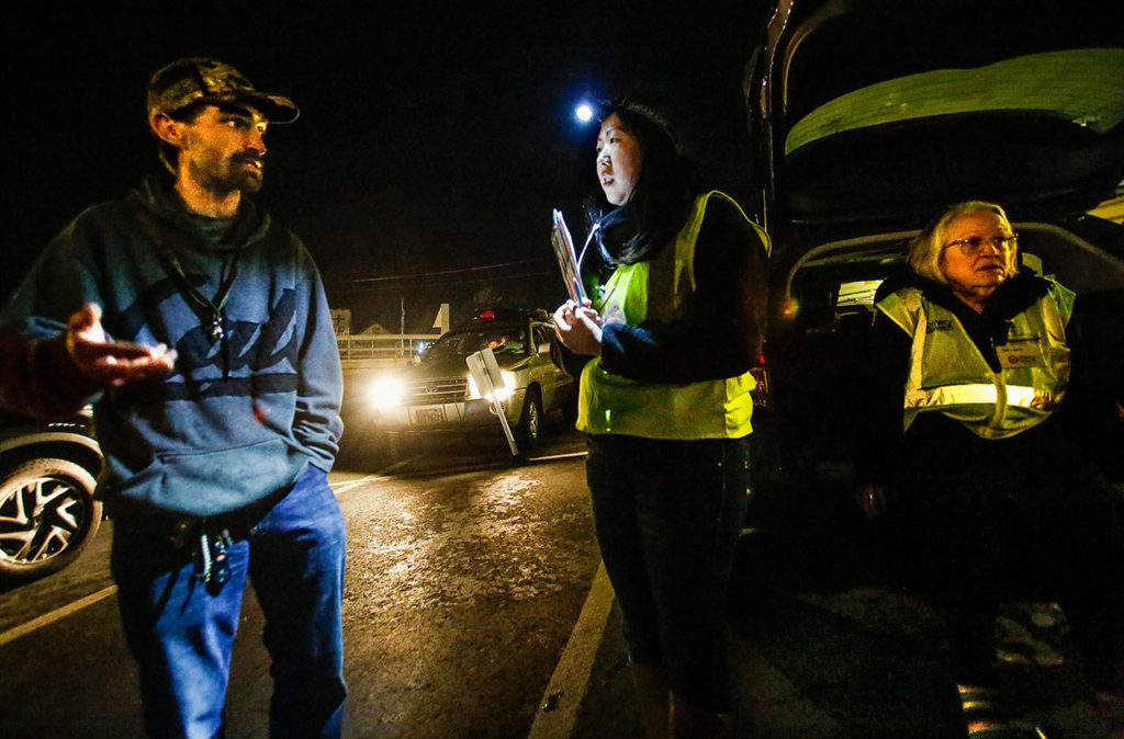 MercyWatch volunteer Amanda Dahl speaks with a man who came for help in a parking lot near the Everett Public Library. Gail Pyper (right) is a school nurse who works with the faith-based effort to help people living on the streets. Dahl acts as her medical scribe. (Dan Bates / The Herald)
